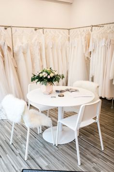 a white table and chairs in front of wedding dresses