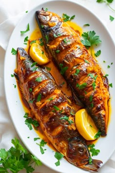 two fish on a white plate with lemons and parsley garnishes