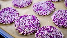 purple sprinkled cookies sitting on top of a cookie sheet