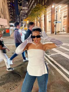 a woman in white shirt and jeans standing on street corner with headphones around her ears