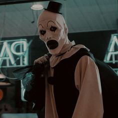 a man wearing a creepy mask and holding a bag in front of a neon sign