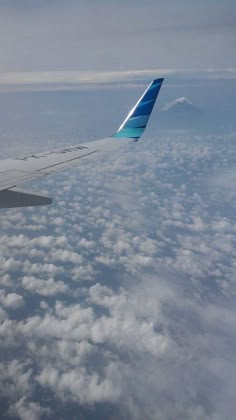 the wing of an airplane flying high above the clouds in the blue and white sky