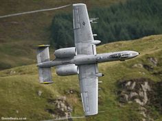 a fighter jet flying through the air over a lush green hillside