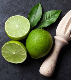 limes with leaves and a wooden spoon on a black surface next to them are cut in half