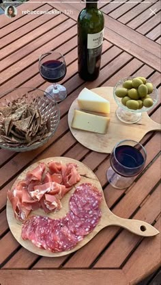 a wooden table topped with cheese and meats next to bottles of wine on top of it