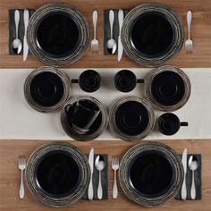 black plates and silverware are arranged on a wooden table with white linen napkins