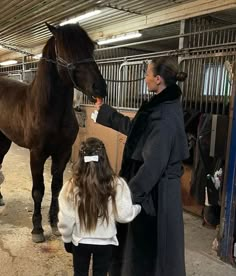 a woman standing next to a brown horse in a stable with another person holding the reins