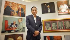 a man standing in front of many paintings on the wall with his hands clasped to his chest