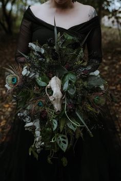 a woman in a black dress holding a bouquet with feathers and flowers on it's side