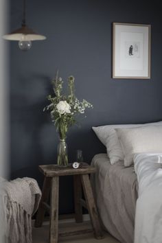 a vase with flowers sitting on top of a wooden table next to a white bed