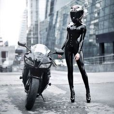 a woman in black catsuit standing next to a motorcycle