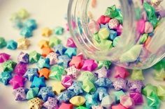 a jar filled with lots of different colored stars next to a pile of smaller ones