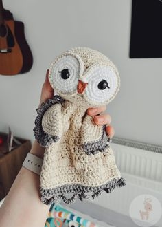 a person holding an owl crocheted stuffed animal in their hand with a guitar on the wall behind them