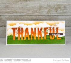 a card with the words thank you in orange and green on it, sitting next to a wooden background