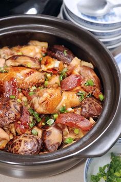 a bowl filled with meat and vegetables on top of a table next to silver plates