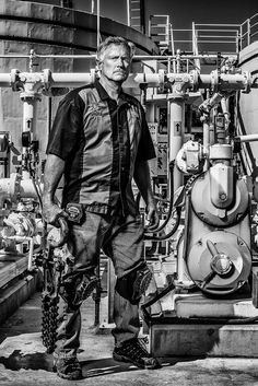 a man standing in front of a machine with lots of pipes and valves on it