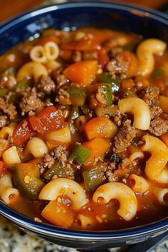 a blue bowl filled with pasta and meat soup on top of a granite countertop