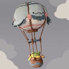 a crocheted hot air balloon flying through the sky with a frog on it