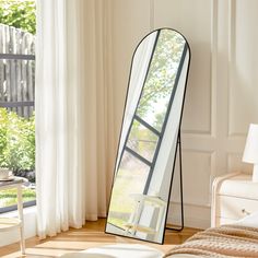 a large mirror sitting on top of a wooden floor next to a white bed in a room