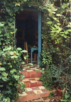 an open door to a small house surrounded by greenery