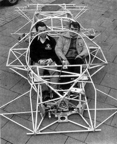 two men are sitting in a large metal structure on the sidewalk while another man stands next to them