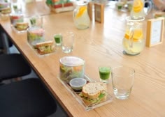 a wooden table topped with sandwiches and glasses filled with juices on top of it