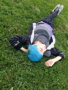 a boy with blue hair laying on the grass