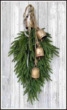 a bunch of bells hanging from a tree branch on a white wooden wall with pine needles