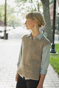 a woman is standing on the side walk wearing a sweater vest and black leggings