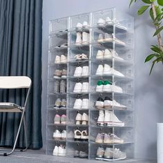 a clear shoe rack with several pairs of shoes on it next to a chair and potted plant