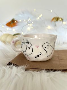 a white cup with ghost faces on it sitting on top of a cardboard box next to christmas lights