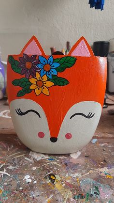 an orange and white painted bowl with flowers on it sitting on a table next to paintbrushes