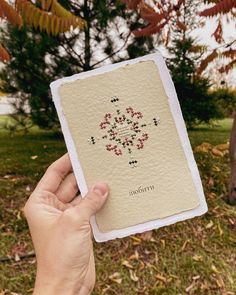 a person holding up a card in front of a tree with leaves and flowers on it