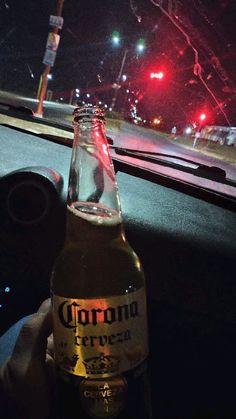 a bottle of corona beer sitting on the dashboard of a car in front of a red light