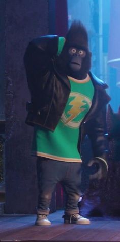 a gorilla in a green t - shirt and black leather jacket standing on a stage