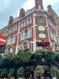 people are standing in front of a building with flowers on the windows and plants growing all over it