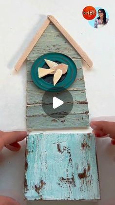 two hands are holding a birdhouse made out of wood