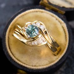 a gold ring with an aqua blue diamond in it sitting on top of a velvet case