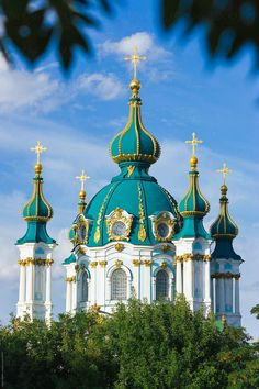 an ornate blue and white church with golden crosses on it's steeple surrounded by trees