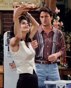 a man and woman standing in front of a refrigerator holding a plate with food on it