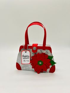 a handbag with a red flower on the front and side, sitting against a white background