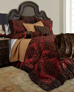 a bed with a red and brown comforter on it next to a night stand