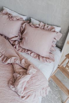 an unmade bed with pink sheets and ruffles on the pillowcase, next to a wooden chair