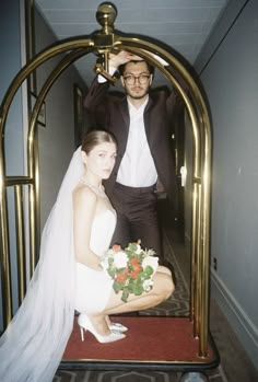 a man standing next to a woman in a wedding dress on a red carpeted hallway