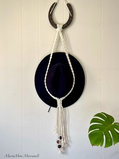 a hat hanging on the wall next to a potted plant with a rope around it