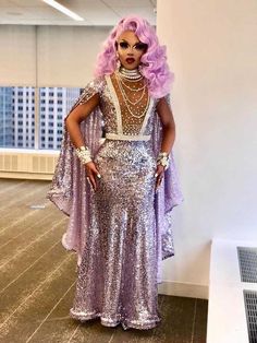 a woman with pink hair wearing a purple dress and pearls on her head standing in an empty room