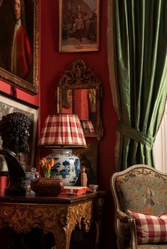 a living room with red walls and paintings on the wall, two chairs in front of a table