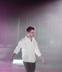 a male in a white shirt and black pants is skating on the ice with his arms out