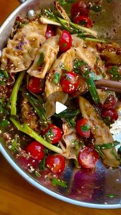 a silver bowl filled with pasta and veggies on top of a wooden table