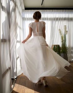 a woman in a white dress is standing near a window